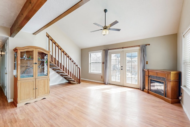 unfurnished living room with lofted ceiling with beams, a premium fireplace, stairs, french doors, and light wood-type flooring