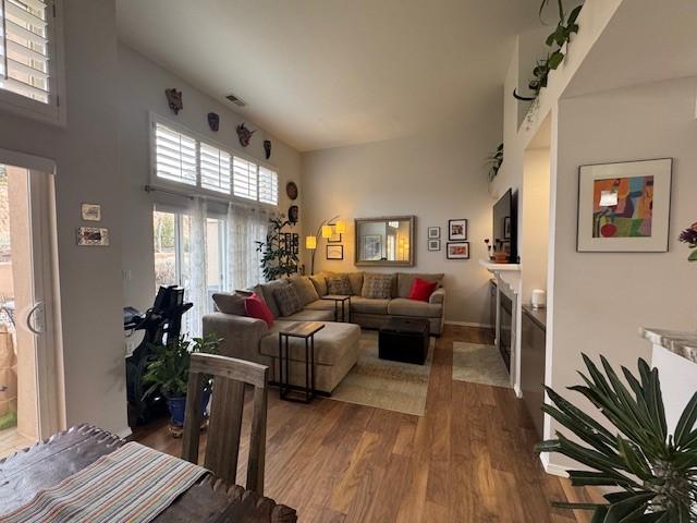 living area with a fireplace with flush hearth, a high ceiling, visible vents, and dark wood-style flooring