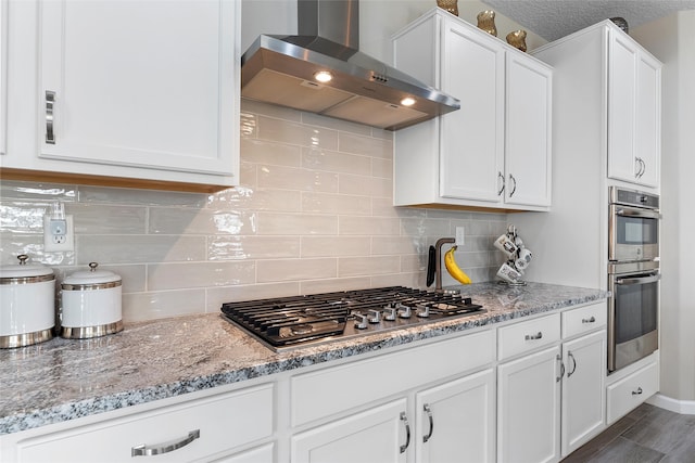 kitchen with wall chimney range hood, appliances with stainless steel finishes, and white cabinetry