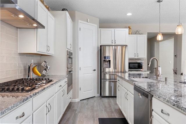 kitchen with wall chimney range hood, white cabinetry, appliances with stainless steel finishes, and a sink