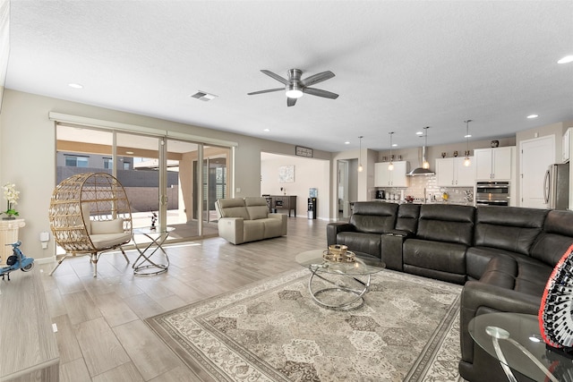 living area with ceiling fan, light wood finished floors, a textured ceiling, and visible vents