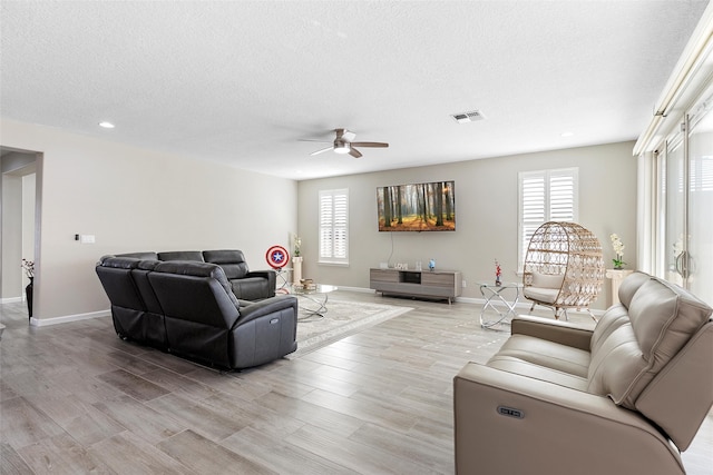 living room featuring baseboards, visible vents, light wood-style flooring, and a textured ceiling