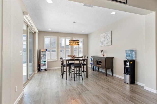 dining area with baseboards, light wood-style flooring, visible vents, and a textured ceiling