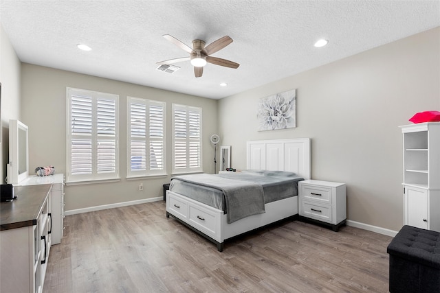 bedroom with baseboards, visible vents, a textured ceiling, and light wood finished floors