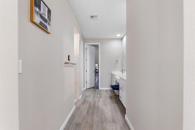 corridor featuring light wood-type flooring, visible vents, a sink, and baseboards