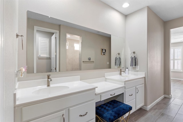 full bath featuring double vanity, wood finish floors, a sink, and baseboards