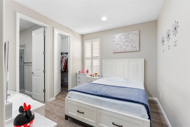 bedroom with a textured ceiling, a spacious closet, baseboards, and wood finished floors