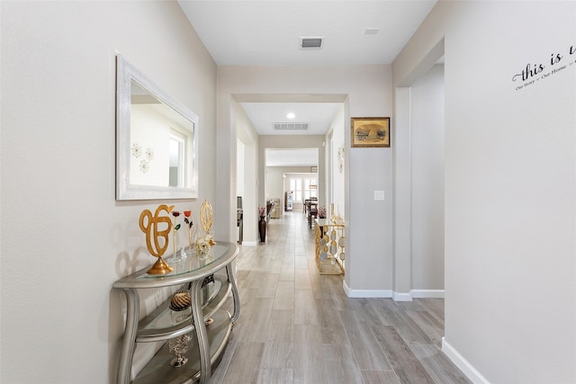 hallway featuring light wood-style floors, visible vents, and baseboards