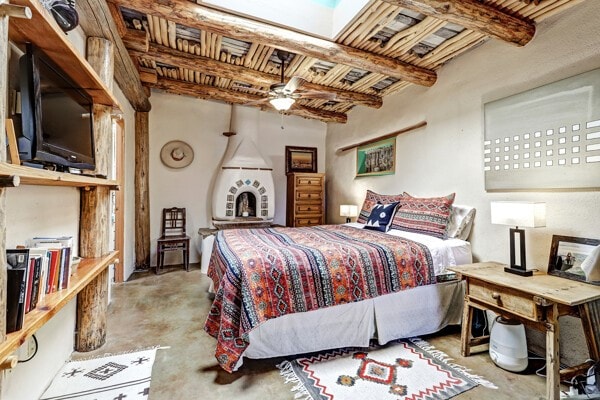 220 Irvine Unit B, Santa Fe, NM 87501 - bedroom with unfinished concrete floors, beamed ceiling, ceiling fan, and a fireplace with raised hearth