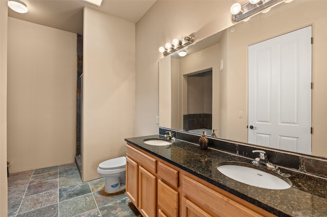 full bathroom featuring toilet, stone finish flooring, double vanity, and a sink