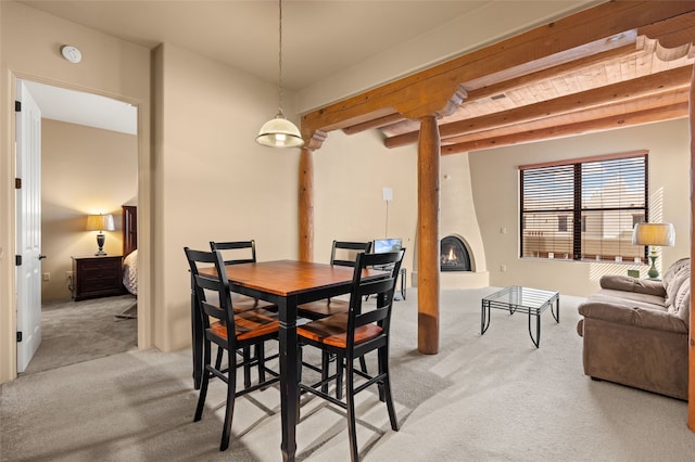 dining area with a large fireplace, light colored carpet, and beamed ceiling