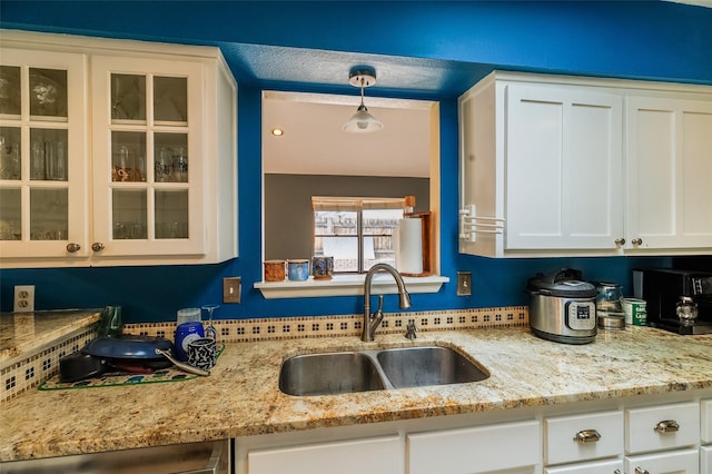 kitchen with light stone counters, a sink, white cabinets, dishwasher, and glass insert cabinets