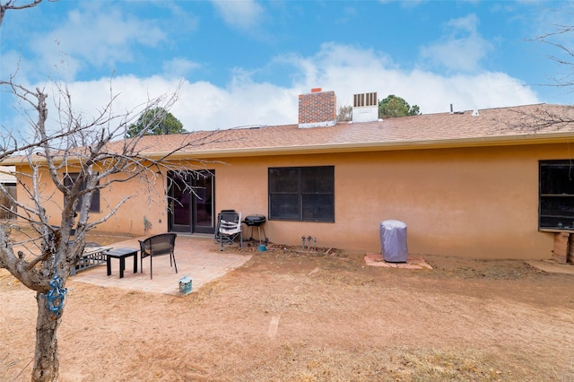 rear view of property featuring a shingled roof, a patio area, a chimney, and stucco siding