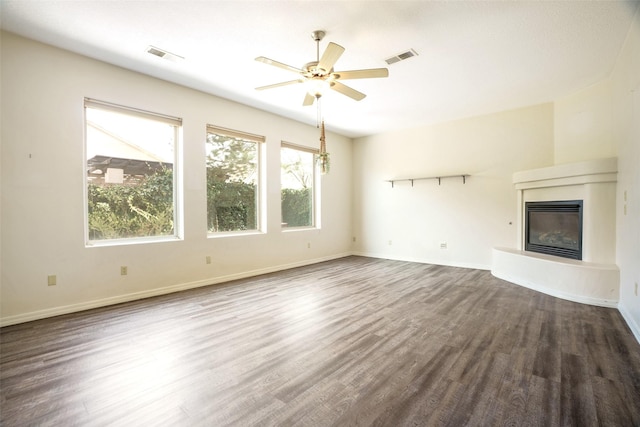 unfurnished living room featuring dark wood-type flooring, a glass covered fireplace, visible vents, and baseboards