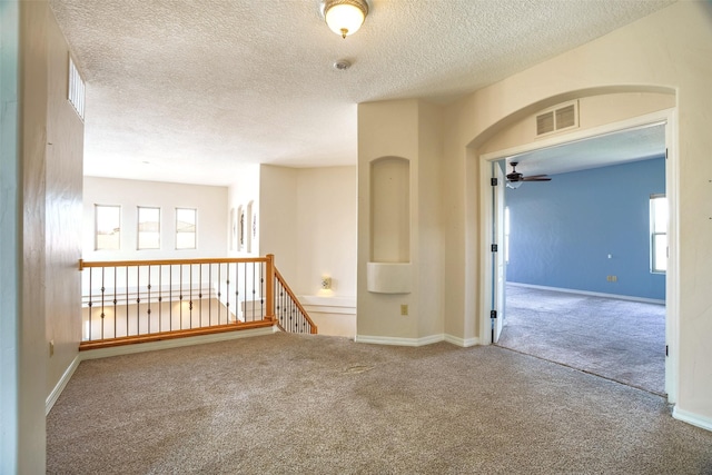 spare room with carpet, visible vents, arched walkways, and baseboards