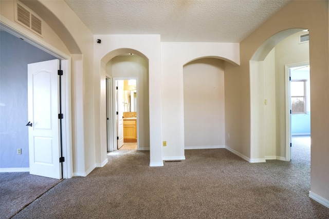 carpeted empty room with a textured ceiling, arched walkways, visible vents, and baseboards