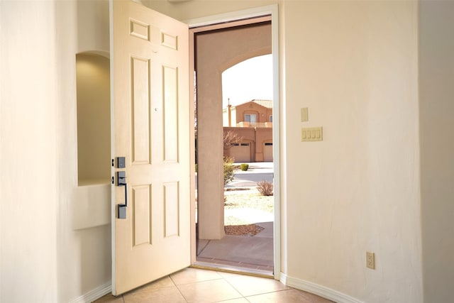 entryway with arched walkways, light tile patterned floors, and baseboards