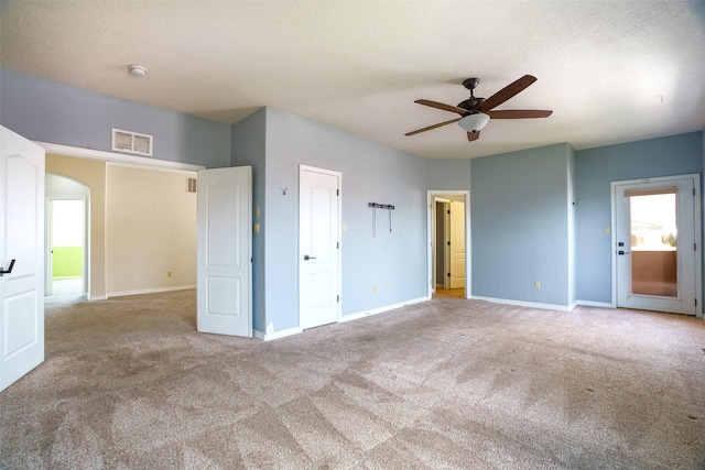 unfurnished bedroom with arched walkways, carpet, visible vents, a textured ceiling, and baseboards