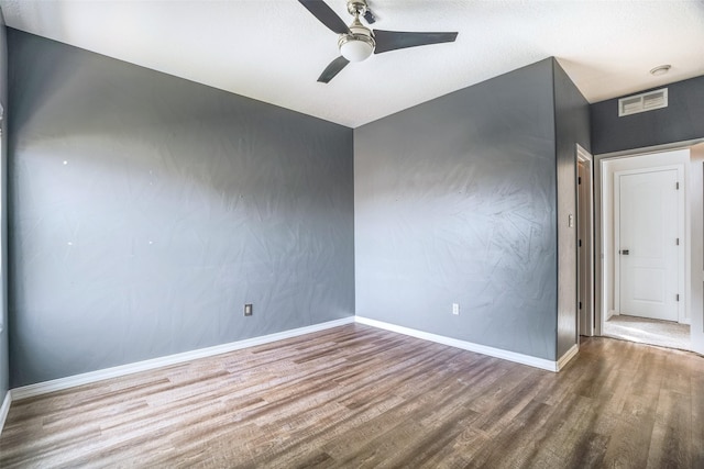 spare room featuring a ceiling fan, visible vents, baseboards, and wood finished floors