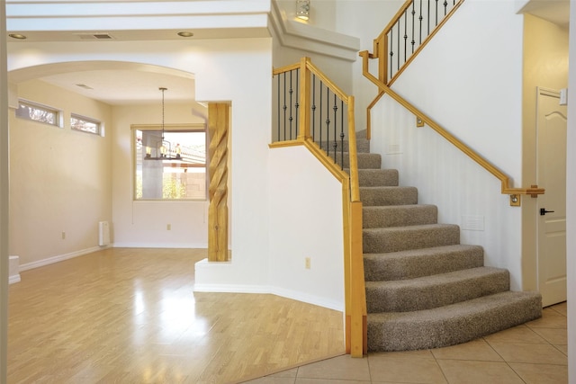 stairway with baseboards, visible vents, arched walkways, wood finished floors, and an inviting chandelier