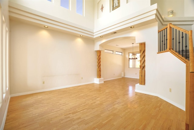 empty room with arched walkways, a notable chandelier, stairway, light wood-style floors, and baseboards