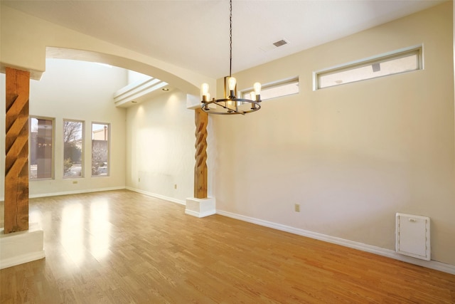 empty room with arched walkways, a notable chandelier, visible vents, wood finished floors, and baseboards