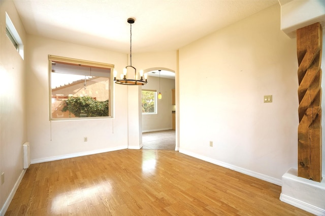 empty room with arched walkways, baseboards, wood finished floors, and a notable chandelier