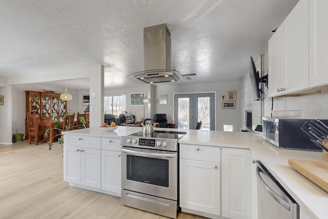 kitchen featuring island range hood, a peninsula, light countertops, appliances with stainless steel finishes, and french doors