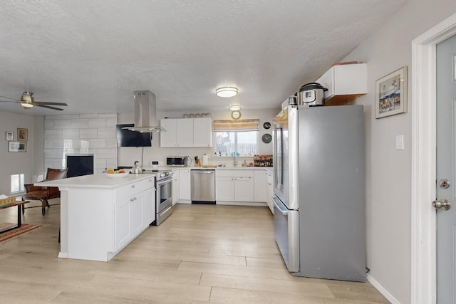 kitchen with appliances with stainless steel finishes, a peninsula, island exhaust hood, light wood-style floors, and white cabinetry