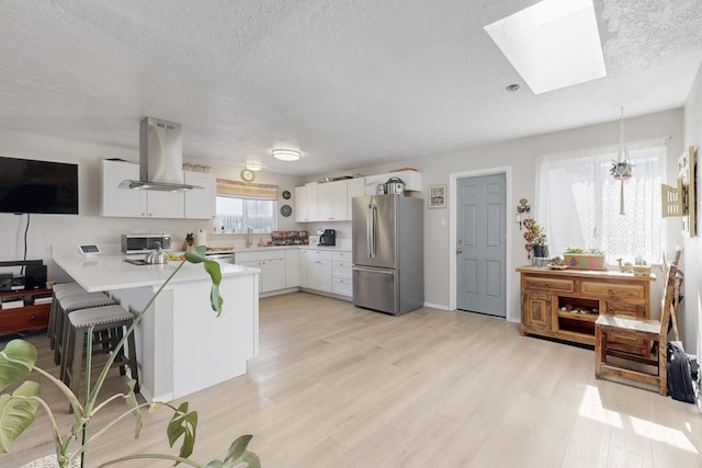 kitchen featuring a peninsula, island exhaust hood, stainless steel appliances, light countertops, and light wood-style floors