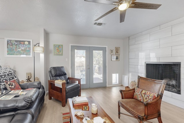 living area featuring visible vents, a tiled fireplace, light wood-style flooring, ceiling fan, and french doors