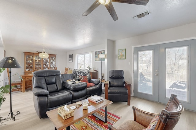 living room featuring light wood-style floors, visible vents, a ceiling fan, and french doors