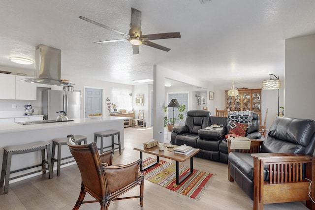 living room with a textured ceiling, ceiling fan, and light wood-type flooring