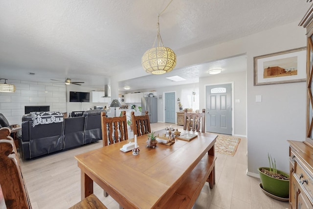 dining area with a skylight, light wood-style floors, ceiling fan, a textured ceiling, and baseboards