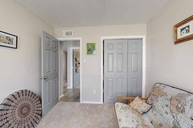 living area featuring a textured ceiling, carpet floors, visible vents, and baseboards