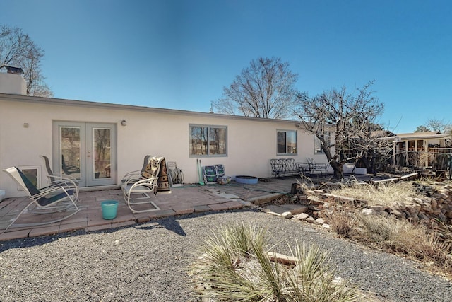 back of house with stucco siding, a chimney, a patio, and french doors