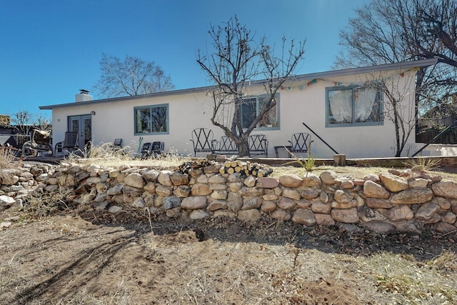 back of property with a chimney, french doors, and stucco siding