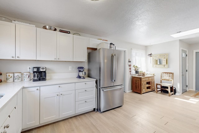 kitchen with light wood-style floors, white cabinetry, light countertops, and freestanding refrigerator