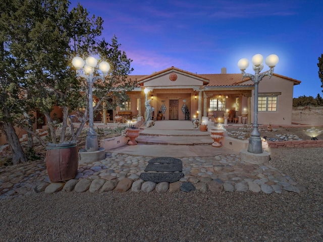 back of house at dusk with a tile roof, a patio area, and stucco siding