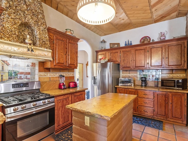 kitchen with tasteful backsplash, vaulted ceiling, arched walkways, and stainless steel appliances