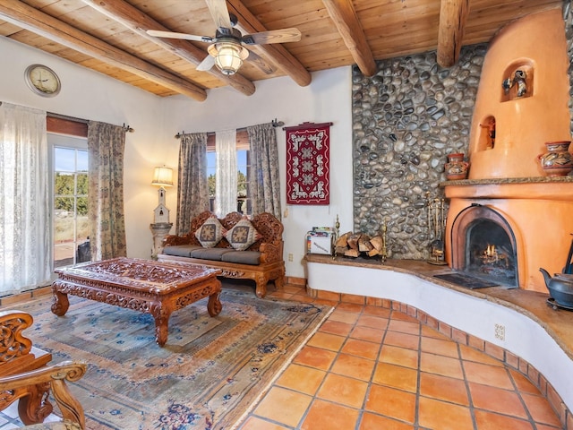 tiled living area with ceiling fan, a lit fireplace, wooden ceiling, and beam ceiling