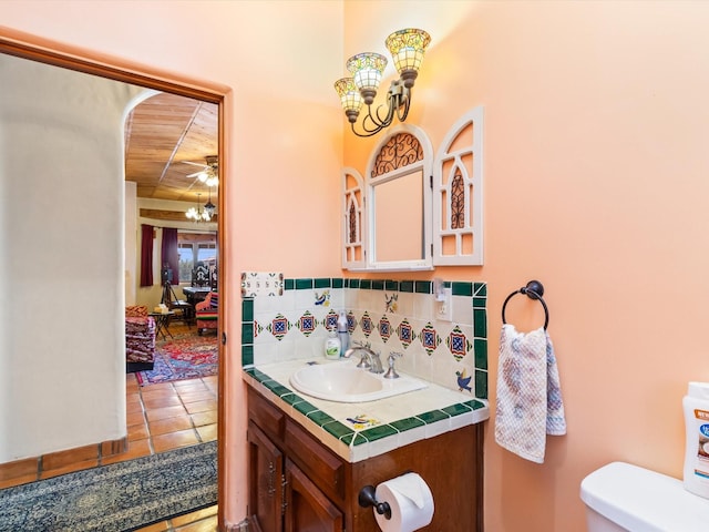 half bath with a chandelier, tasteful backsplash, vanity, and toilet