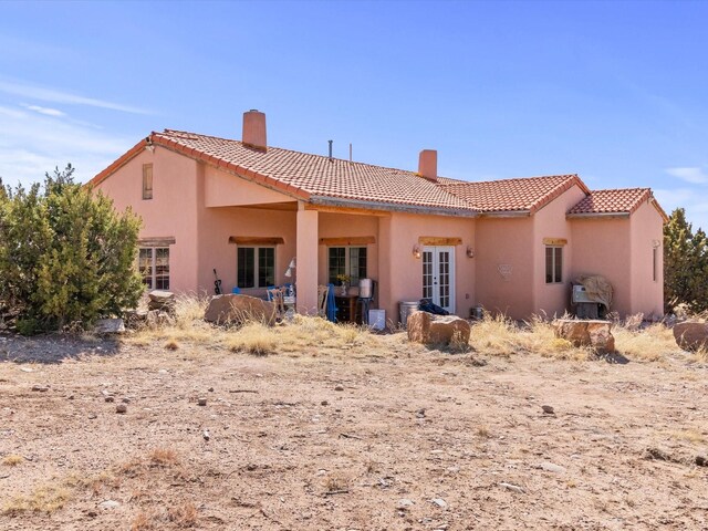 rear view of house featuring a tiled roof, a chimney, and stucco siding