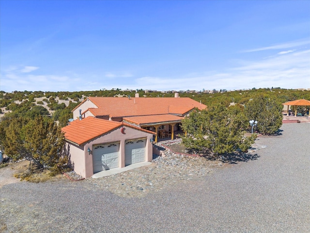 view of front of home featuring an attached garage, a tiled roof, gravel driveway, and stucco siding