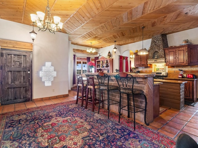 kitchen featuring a chandelier, a breakfast bar, wood ceiling, tile patterned floors, and brown cabinetry