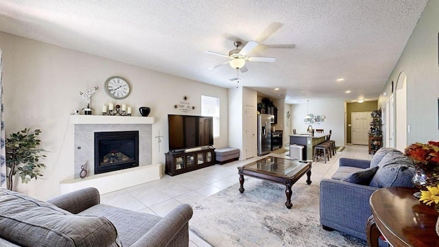 living area with a ceiling fan, light tile patterned flooring, a textured ceiling, and a tiled fireplace