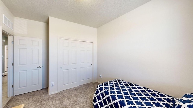 bedroom featuring a closet, light carpet, visible vents, and a textured ceiling