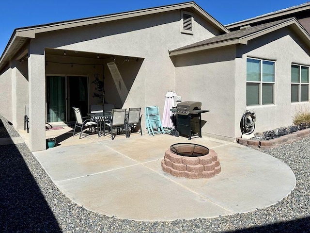 rear view of property with stucco siding, an outdoor fire pit, outdoor dining space, and a patio