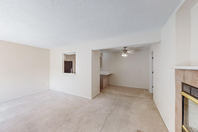 unfurnished living room featuring a textured ceiling, a tiled fireplace, a ceiling fan, and light colored carpet