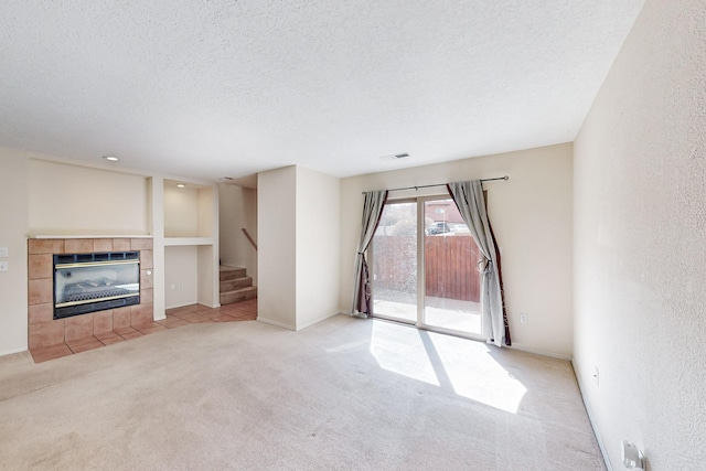 unfurnished living room with carpet floors, visible vents, stairway, a textured ceiling, and a tile fireplace